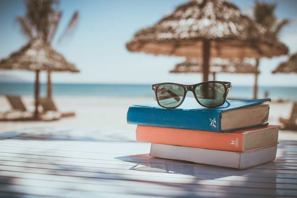 A stack of 3 Books at the beach with sunglasses on top.  Books read :  Healthy Beliefs, Courage and Advocacy for Kind People, and Lead Yourself.  
