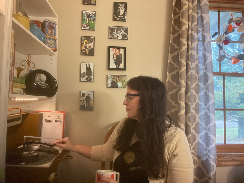 Coach Tina playing a record on the record player holding a cup of coffee