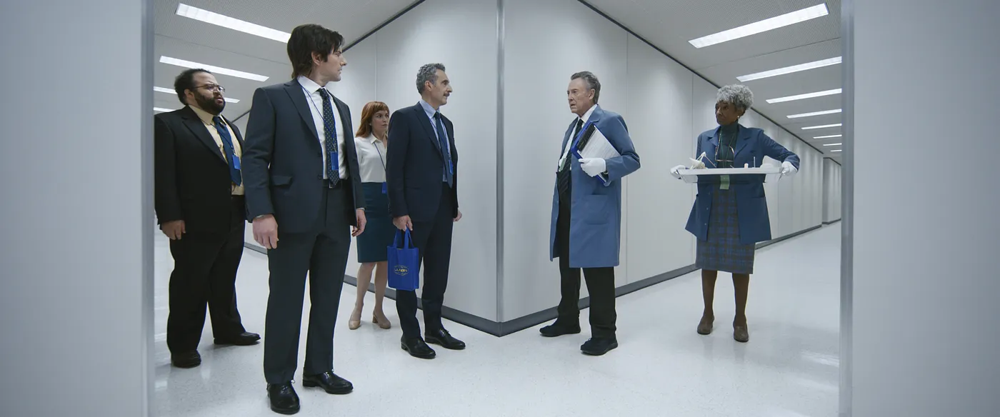 Picture from the TV Series Severance, showing workers standing in a bleak, grey hallway